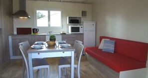 Une cuisine compacte comprenant une table à manger, des chaises, un canapé rouge, un four à micro-ondes, un réfrigérateur et une fenêtre laissant entrer la lumière naturelle.