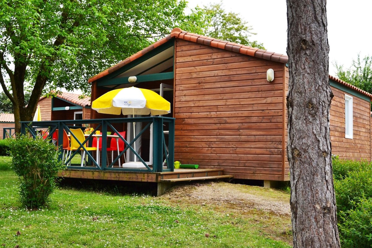 A wooden cabin with a porch, a yellow and white umbrella, and a small table with chairs.