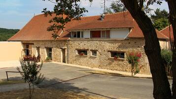 A two-story stone building with a red-tiled roof, a small front garden, and a paved driveway.