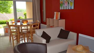 A living room with a white sofa, brown armchair, and a dining area with wooden chairs and a table.