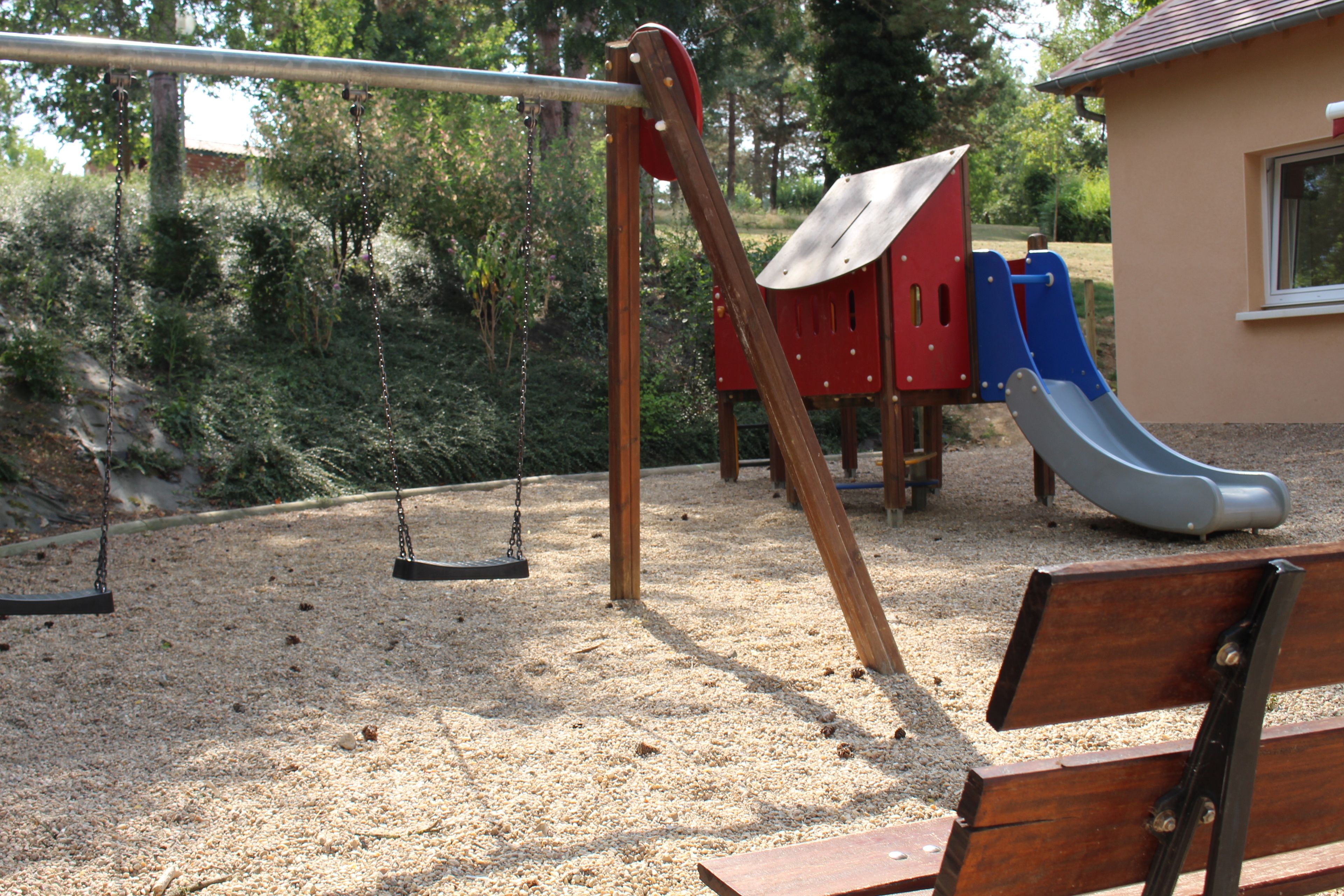 Une aire de jeux avec des balançoires, un toboggan et un banc.
