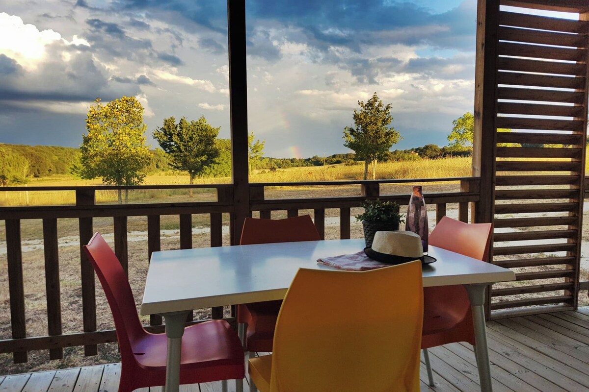 A wooden deck with a table and chairs, a bottle, and a hat on the table.