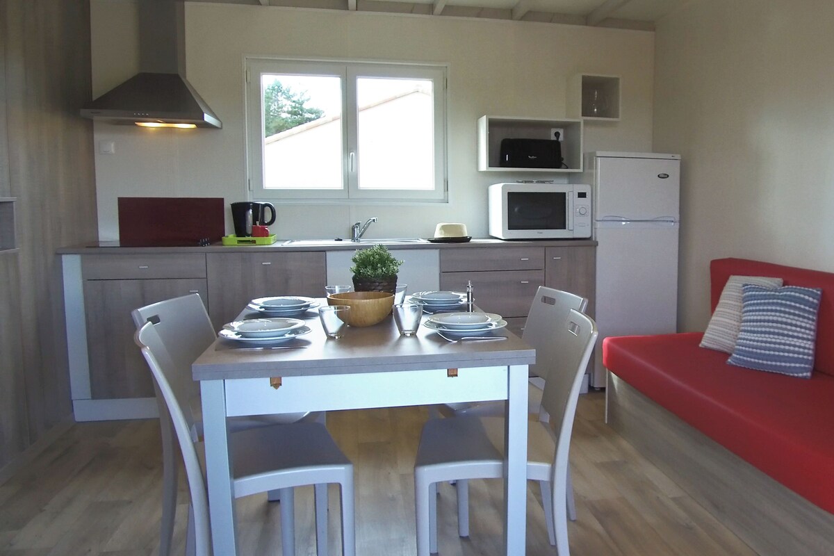 A compact kitchen with a dining table, chairs, a red sofa, and a microwave.