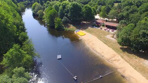 An aerial view of a riverside property with a sandy beach, a small dock, and a building with outdoor seating. - VVF Vienne Poitou, la Bussière (La Bussiere)