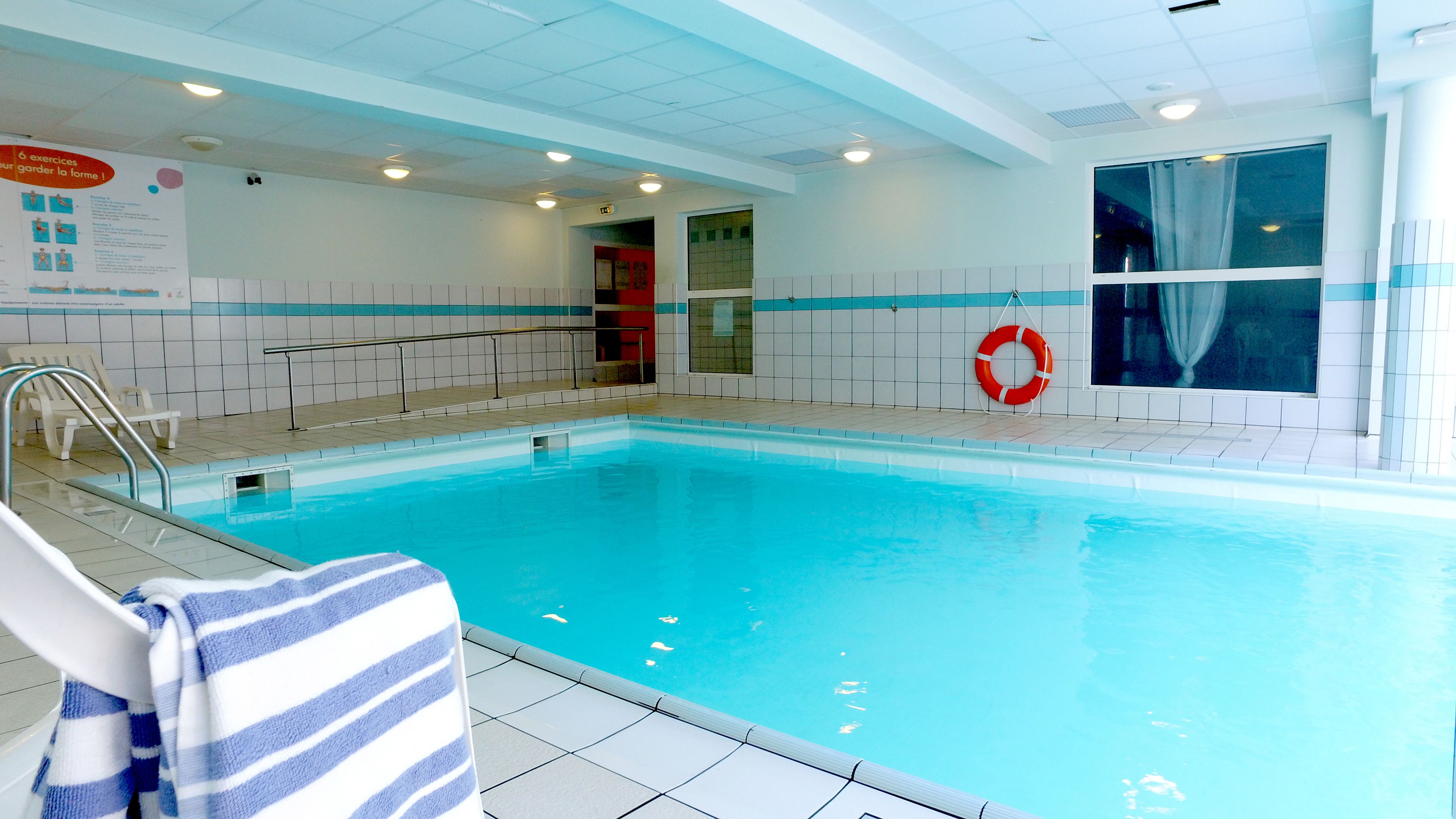 An indoor swimming pool with clear water, tiled walls, and a lifebuoy.