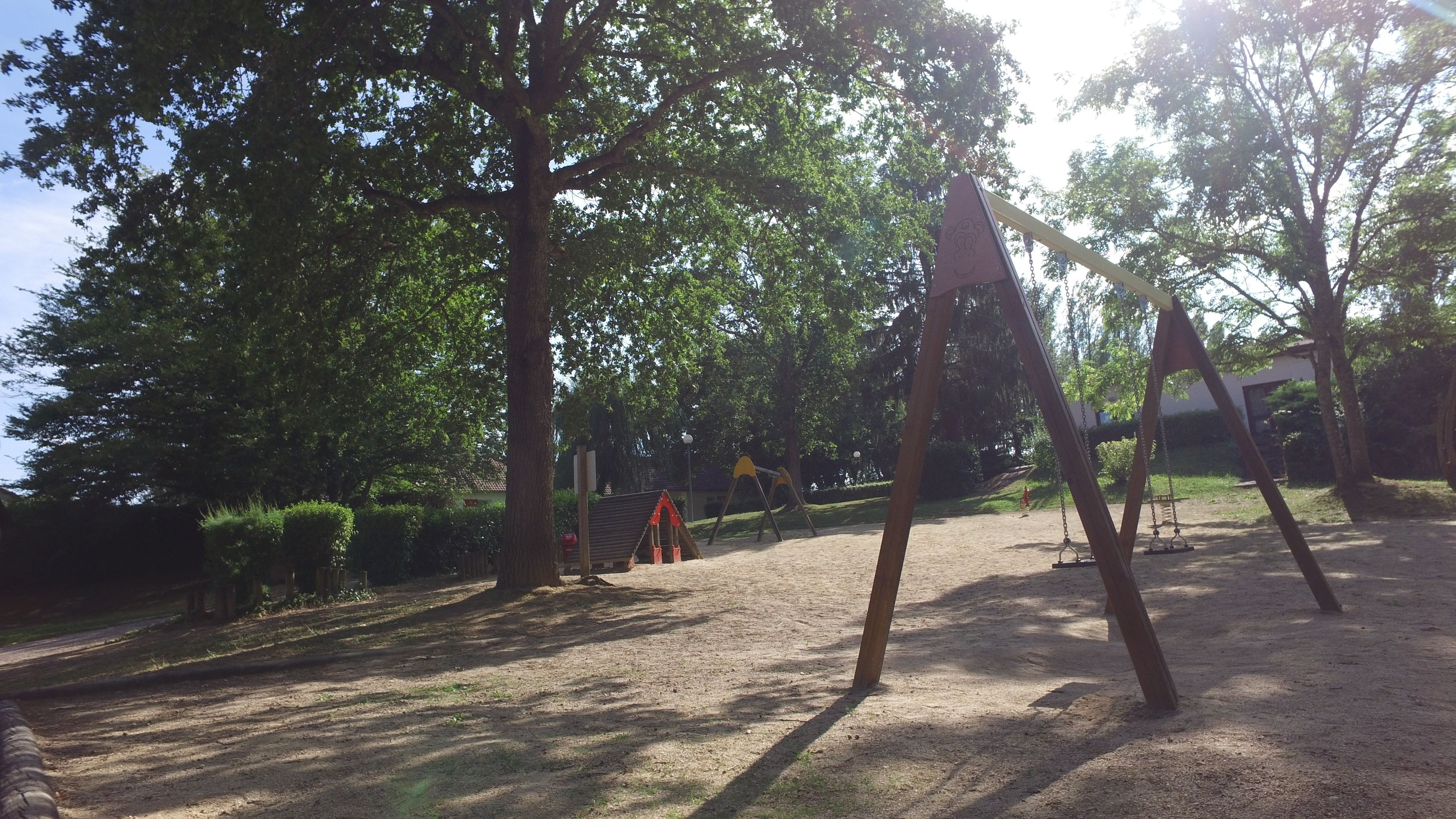 A playground with swings and a slide, surrounded by trees and a grassy area.