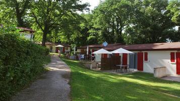 Een rij gelijkvloerse bungalows met buiten zitplaatsen en parasols, omringd door weelderige begroeiing.