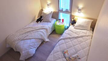 Ein kleines, gemütliches Schlafzimmer mit zwei Betten, einem grünen Hocker und einem Teddybär.