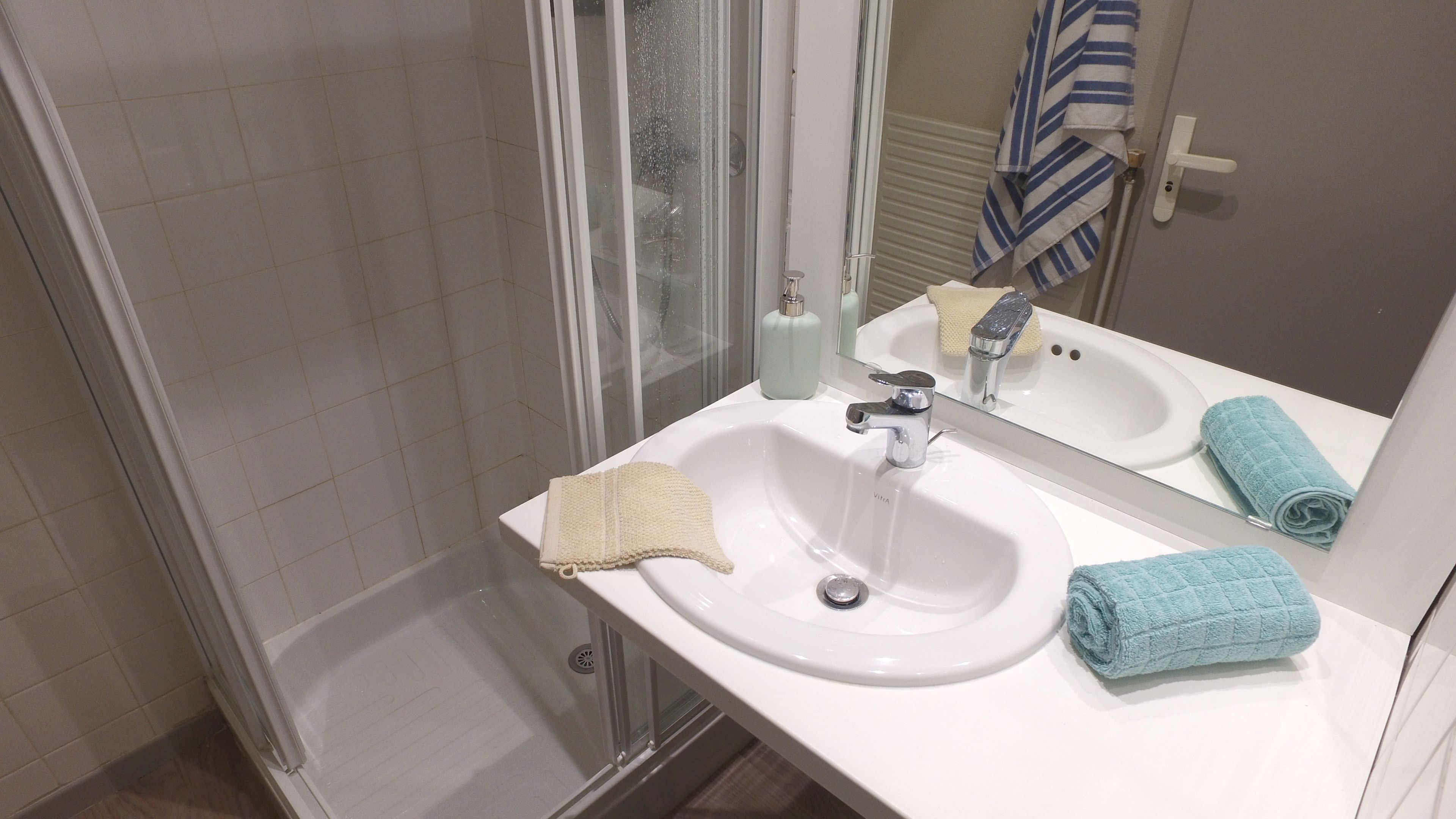 A bathroom with a glass-enclosed shower, a white sink, and a mirror.