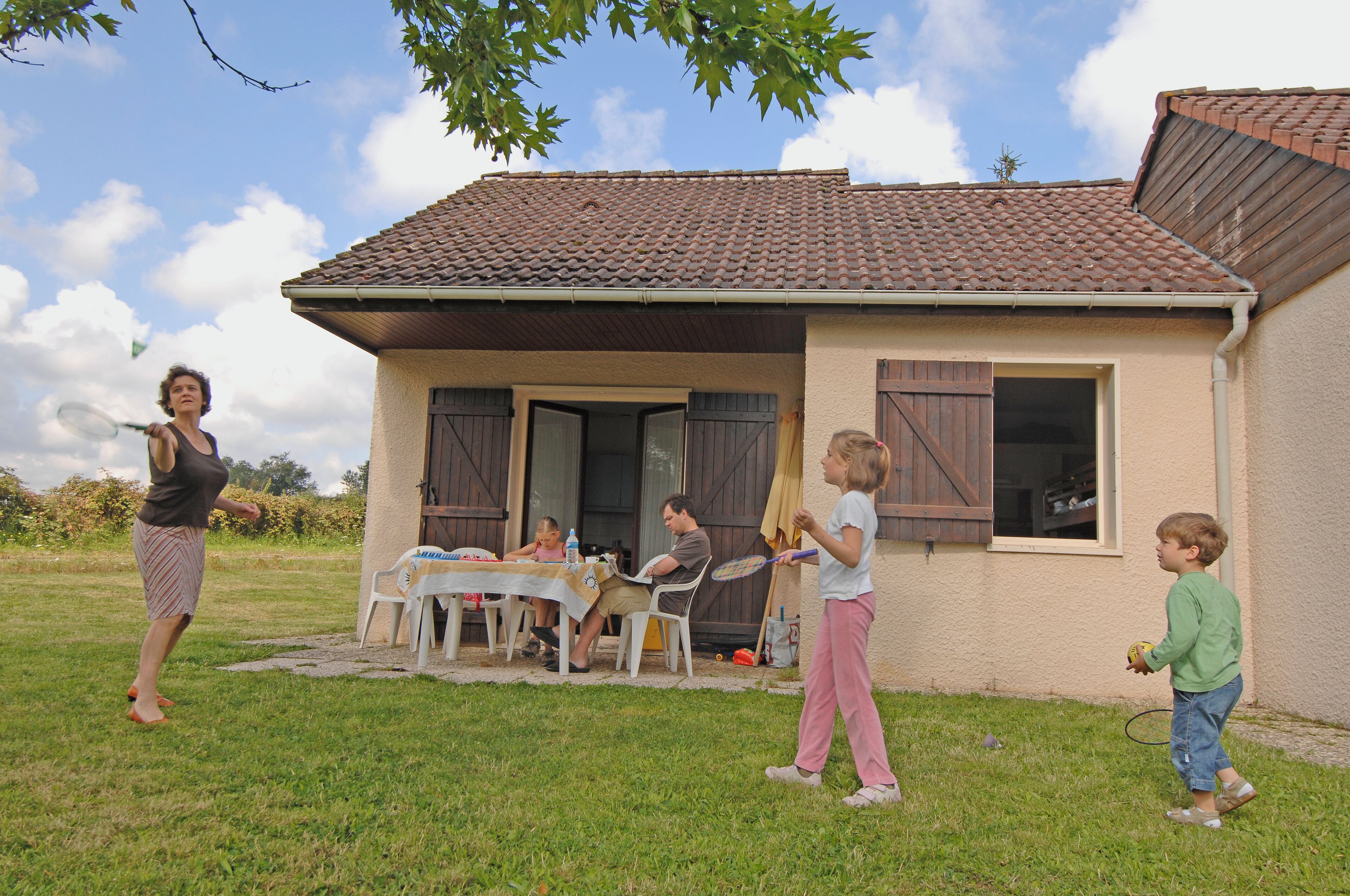 A house with a tiled roof, a front door, and a small porch area with a table and chairs.