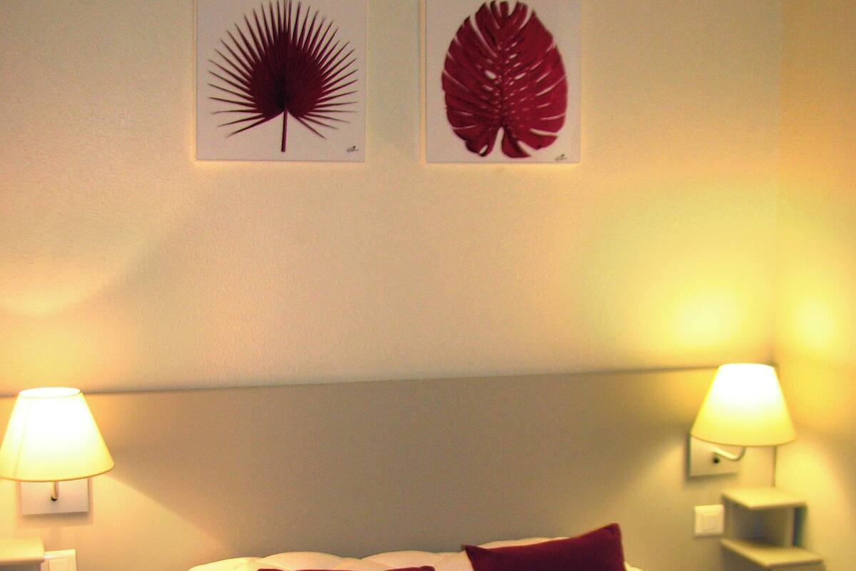 A neatly made bed with white bedding and two red pillows, flanked by two bedside lamps on white nightstands.