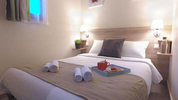 A neatly made bed with rolled towels, a tray with a mug and snacks, and two wall-mounted lamps.
