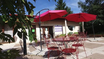 Un espace extérieur aménagé avec des chaises et des tables en métal rouge, entouré de parasols rouges, sous un ciel dégagé.