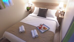 A neatly made bed with white linens, two pillows, a tray with a mug, a cookie, and two rolled towels. - VVF Bourgogne Auxois Morvan, Semur en Auxois (Le Val-Larrey)