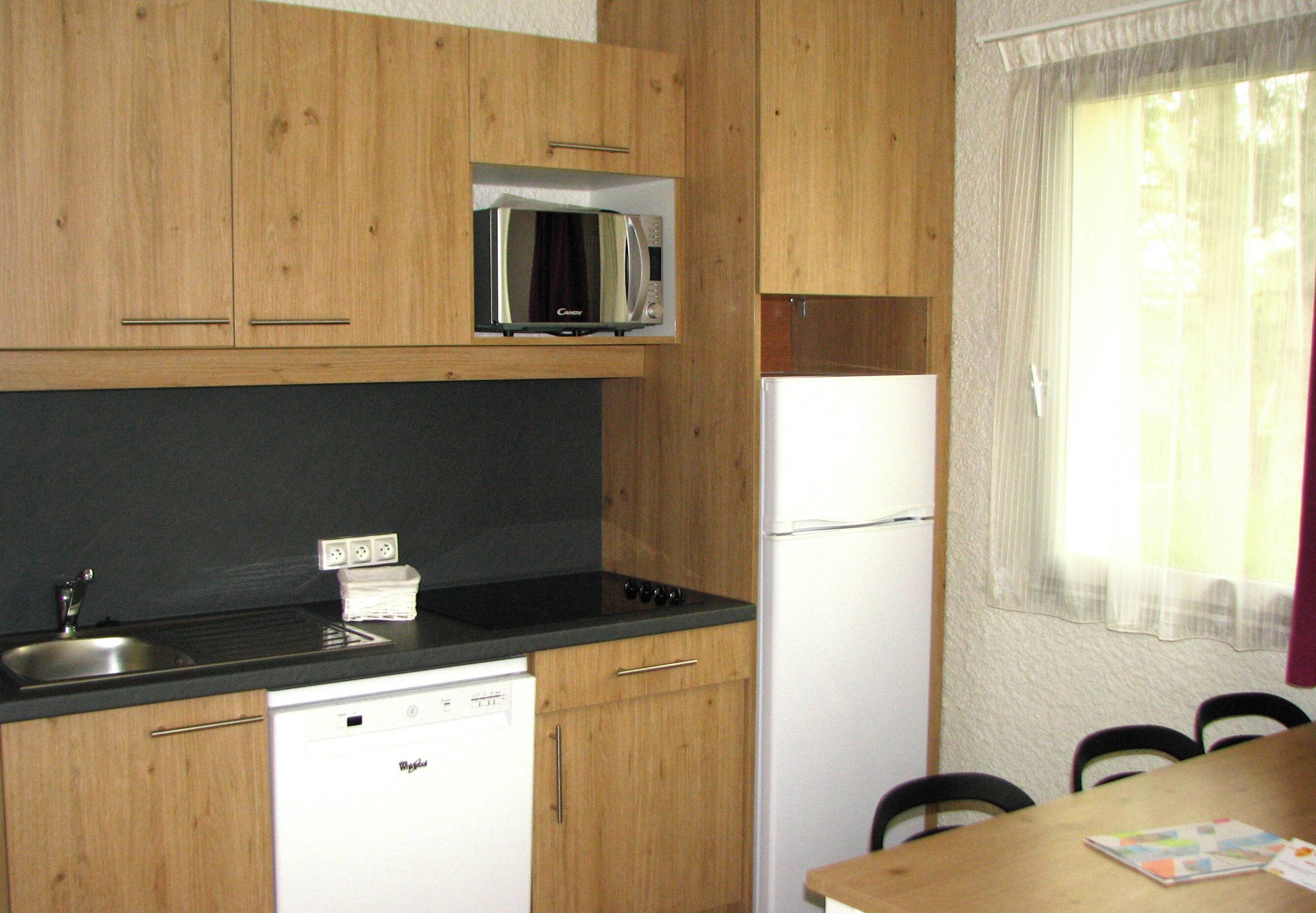 A compact kitchen with wooden cabinets, a microwave, a dishwasher, and a refrigerator.