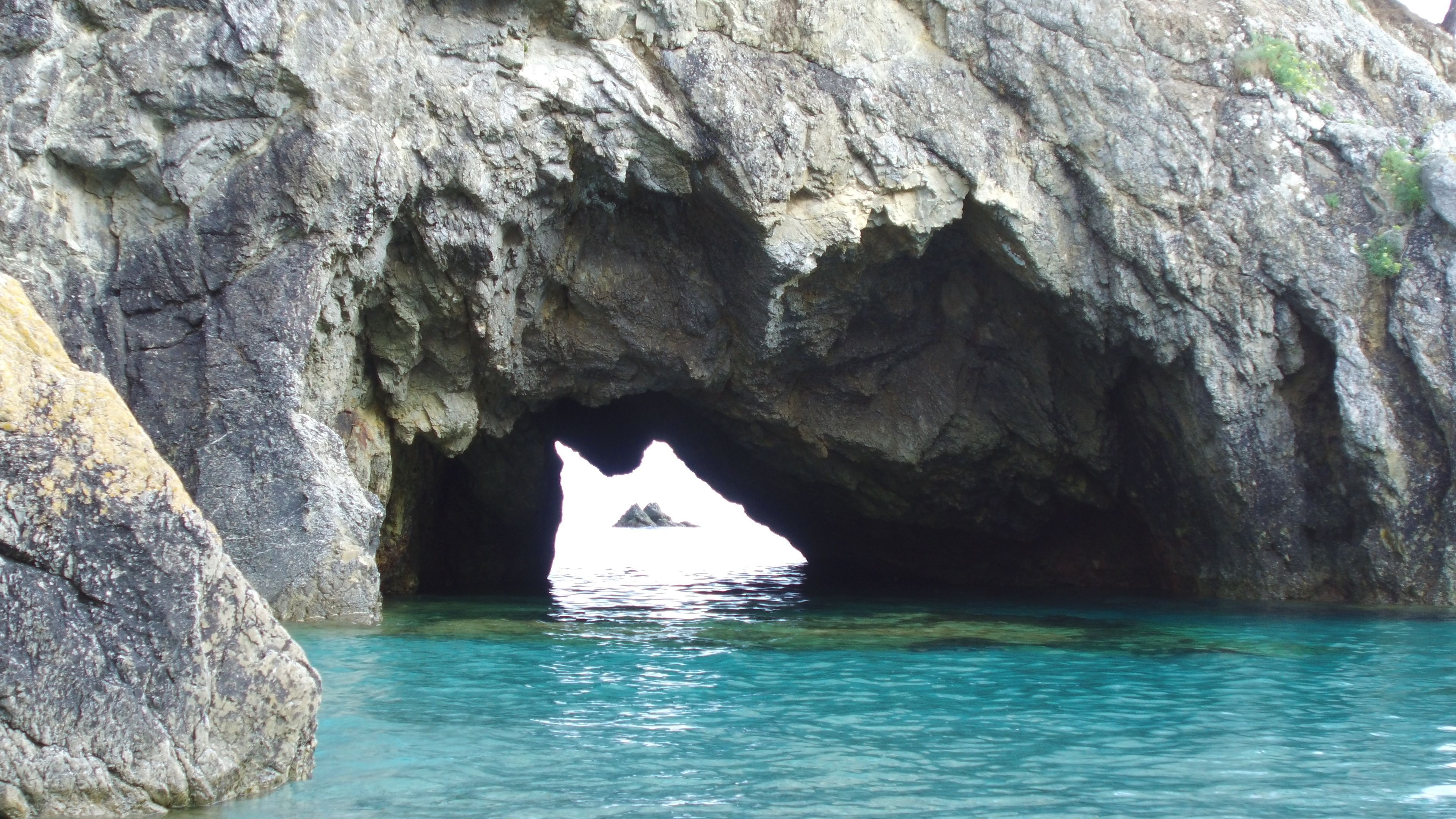 L’entrée d’une grotte rocheuse, avec une eau turquoise et limpide.