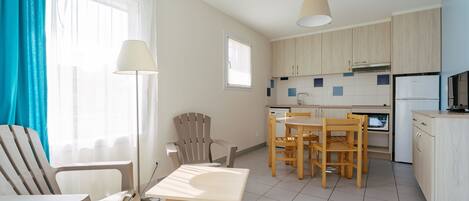 A modern kitchen with wooden cabinets, a dining area with a table and chairs, and a bright window with curtains.
