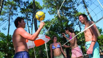 Un groupe de personnes joue au volleyball à l’extérieur, avec des arbres en arrière-plan.