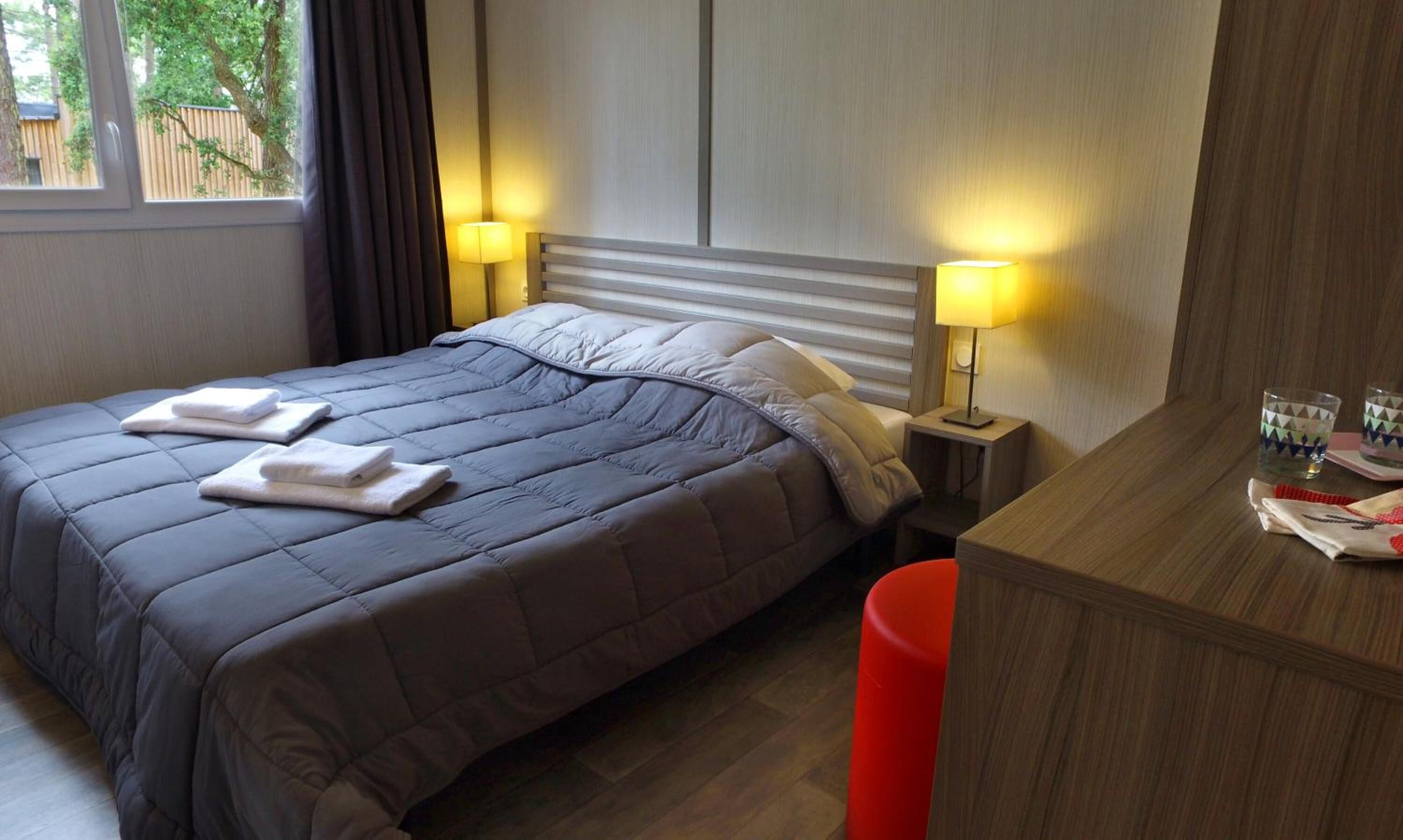 Habitación de hotel con una cama grande, dos lámparas de noche, un escritorio de madera y un cubo de basura rojo.