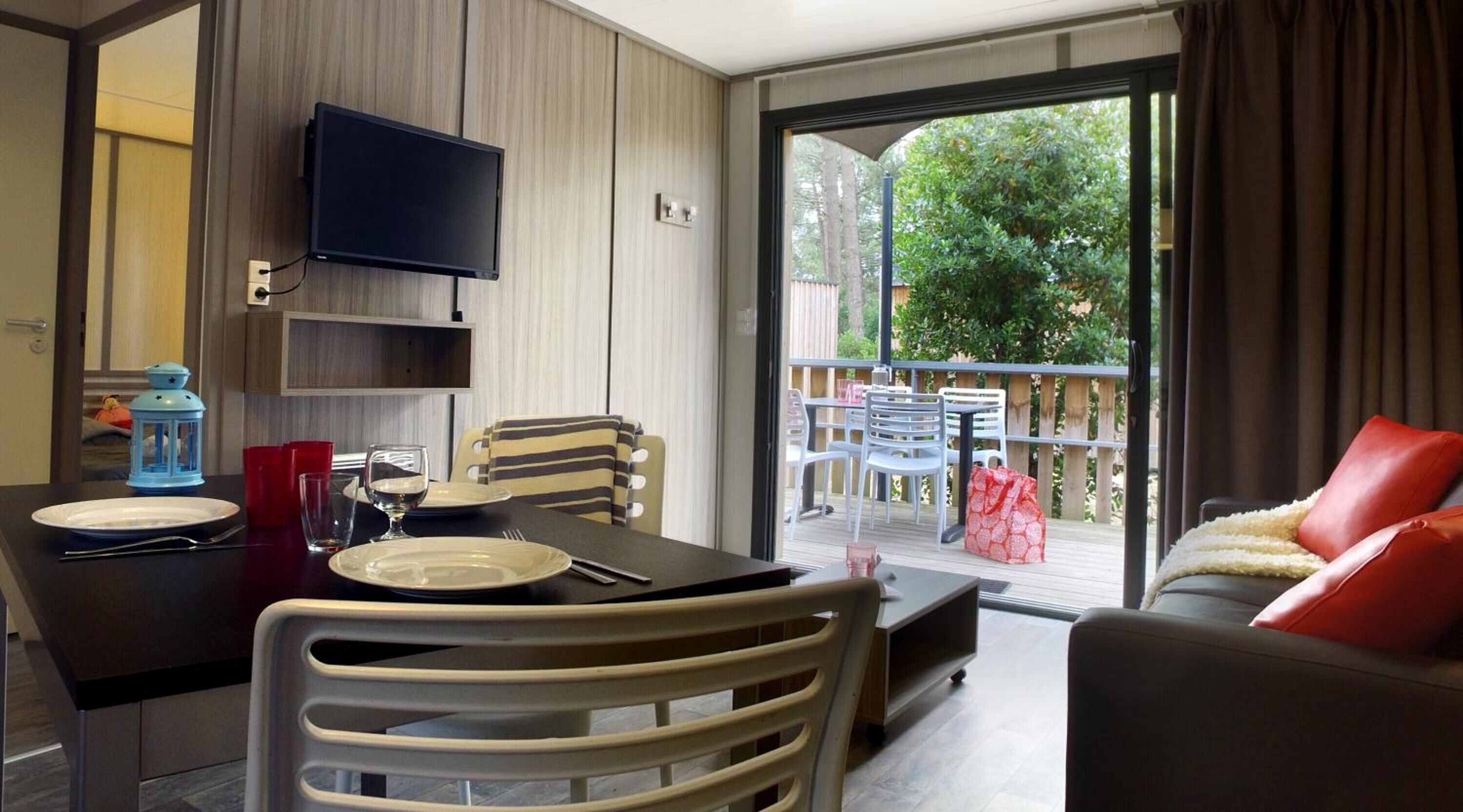 Une chambre moderne dotée d’une table à manger, de chaises, d’un téléviseur fixé au mur et d’un balcon aménagé avec du mobilier d’extérieur.