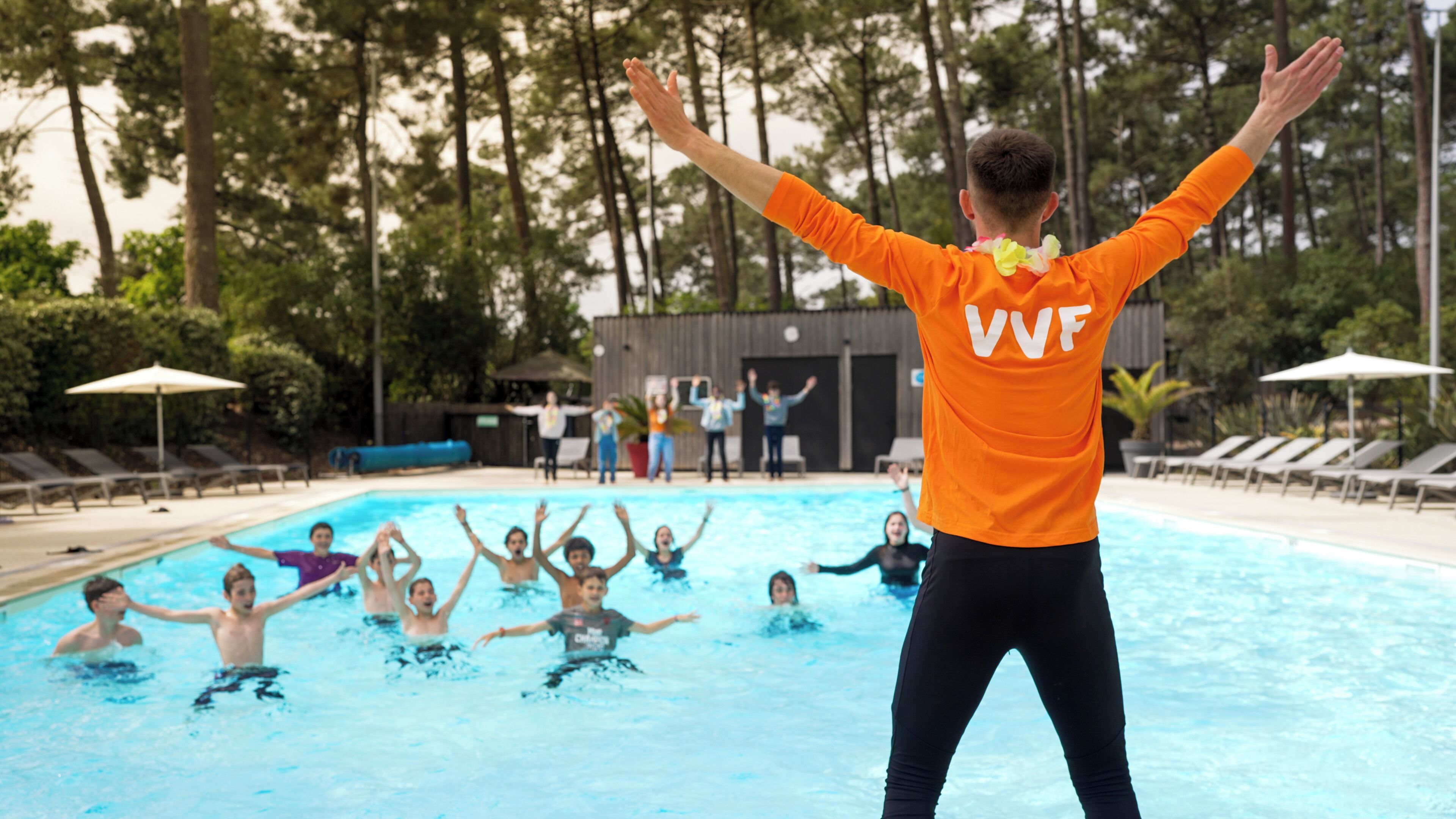 A swimming pool with people in the water and a person standing in the pool with arms raised.