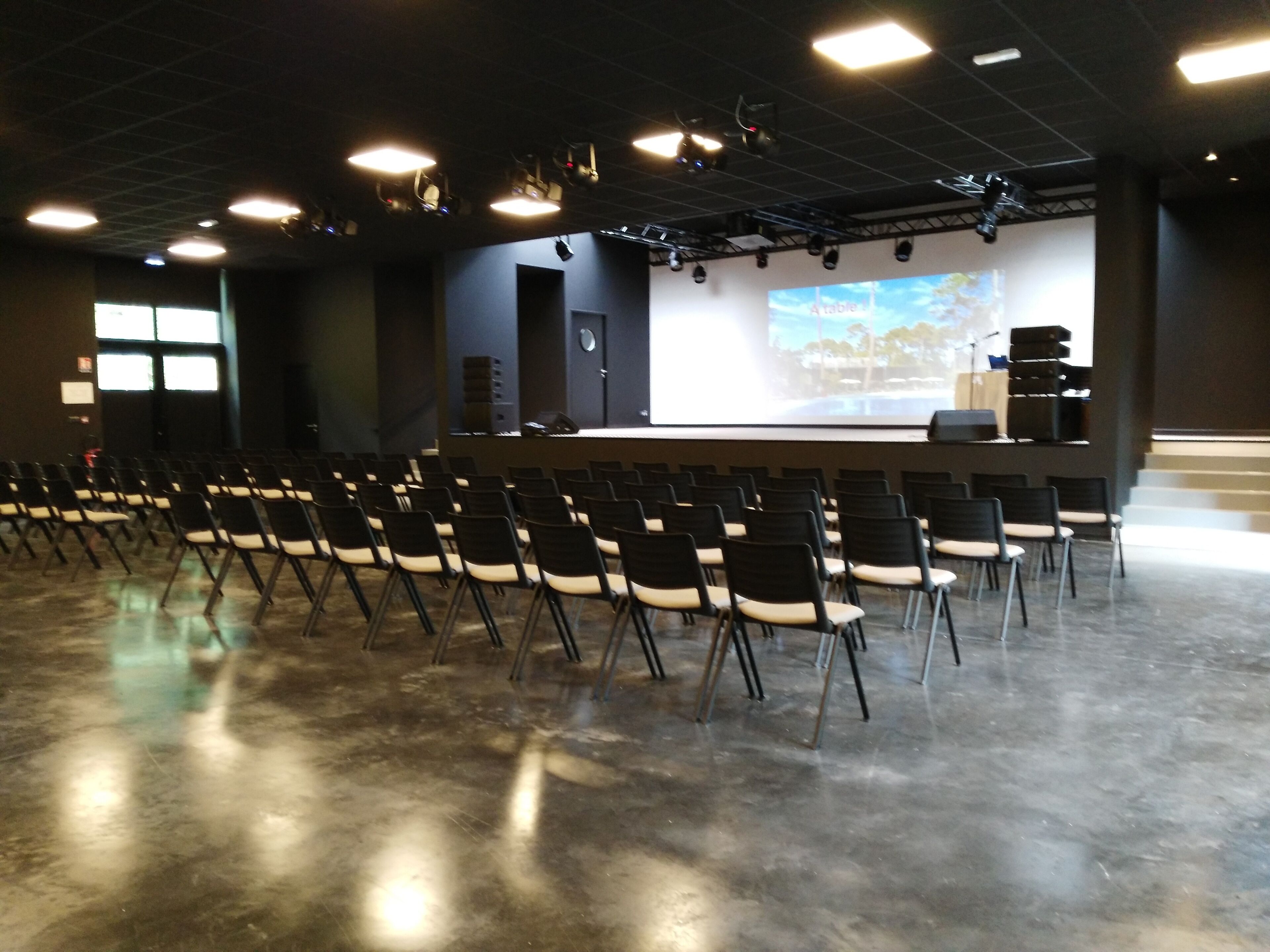 A conference room with rows of chairs facing a stage with a large screen.