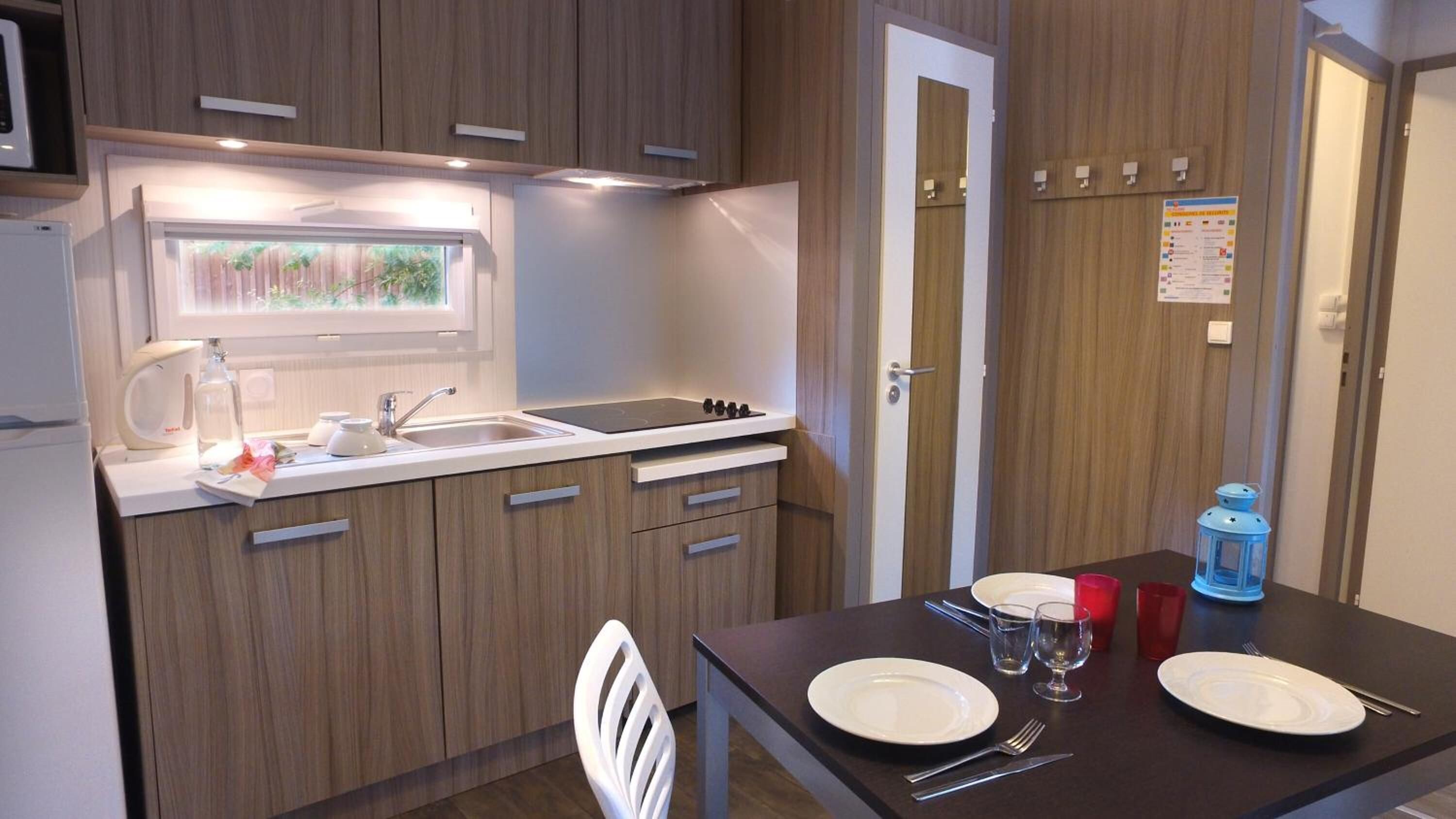 Cocina compacta con fregadero, estufa y ventana. Se aprecia una mesa de comedor con platos y cubiertos.