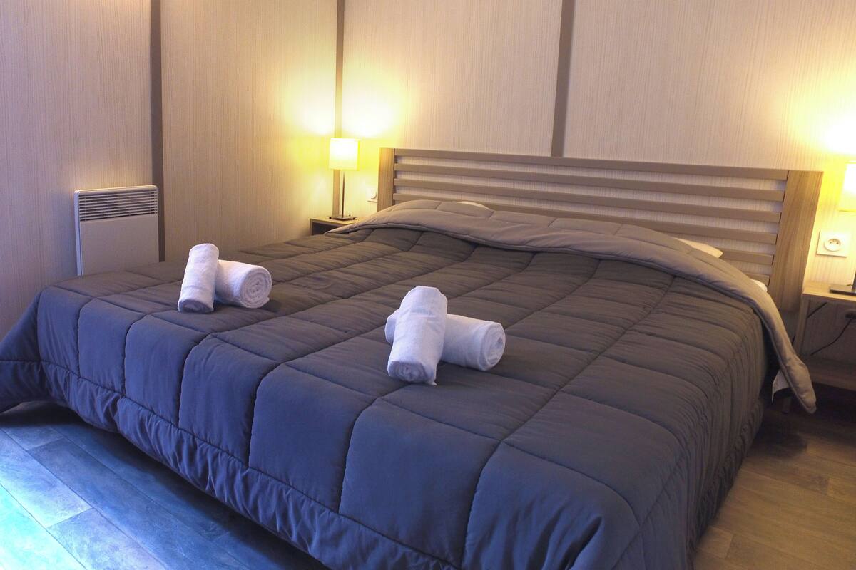 Ein ordentlich bezogenes Bett mit einer dunkelblauen Steudecke und zwei aufgerollten Handtüchern an der Seite.