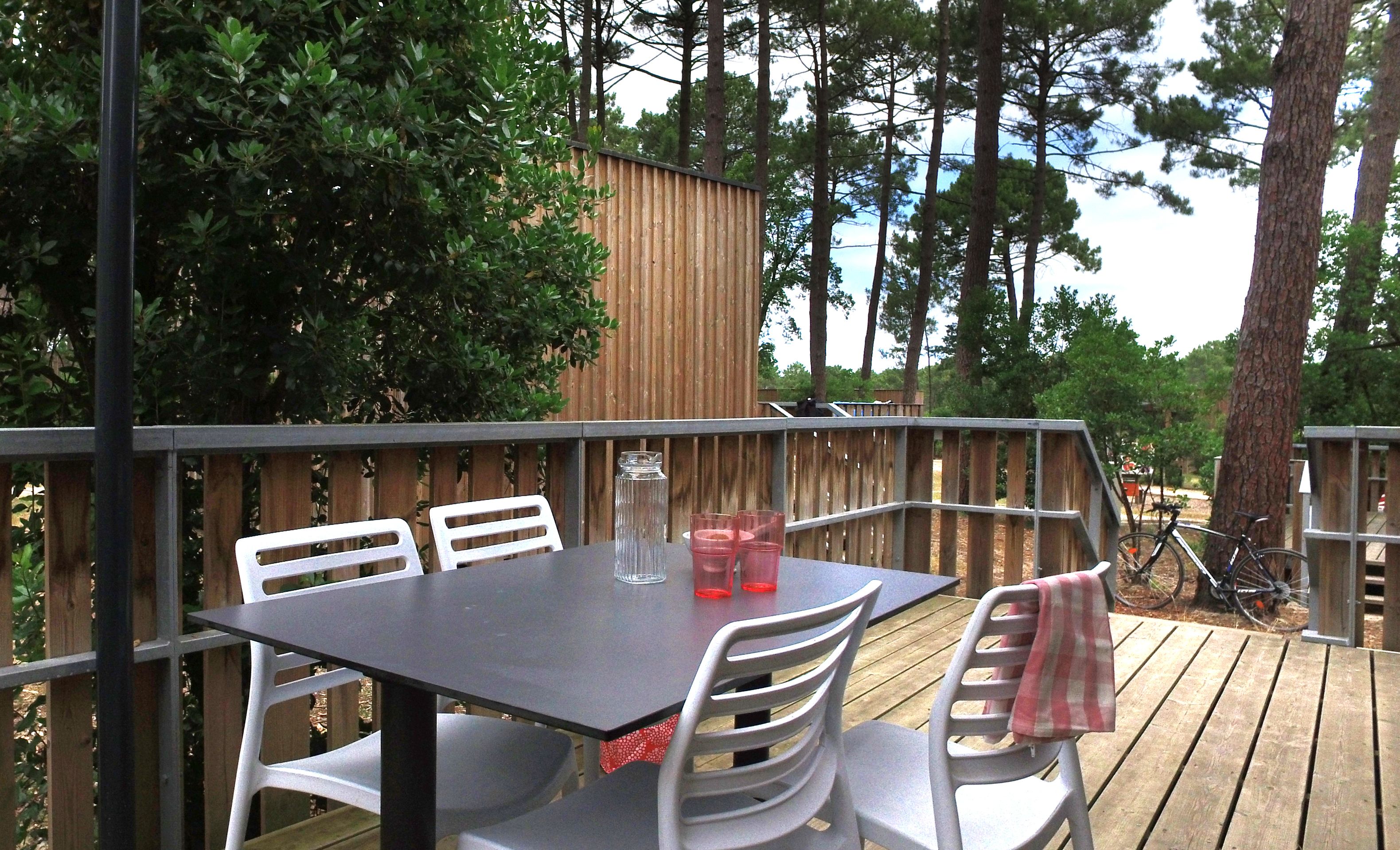 An outdoor patio with a table and chairs, surrounded by a wooden deck and trees.