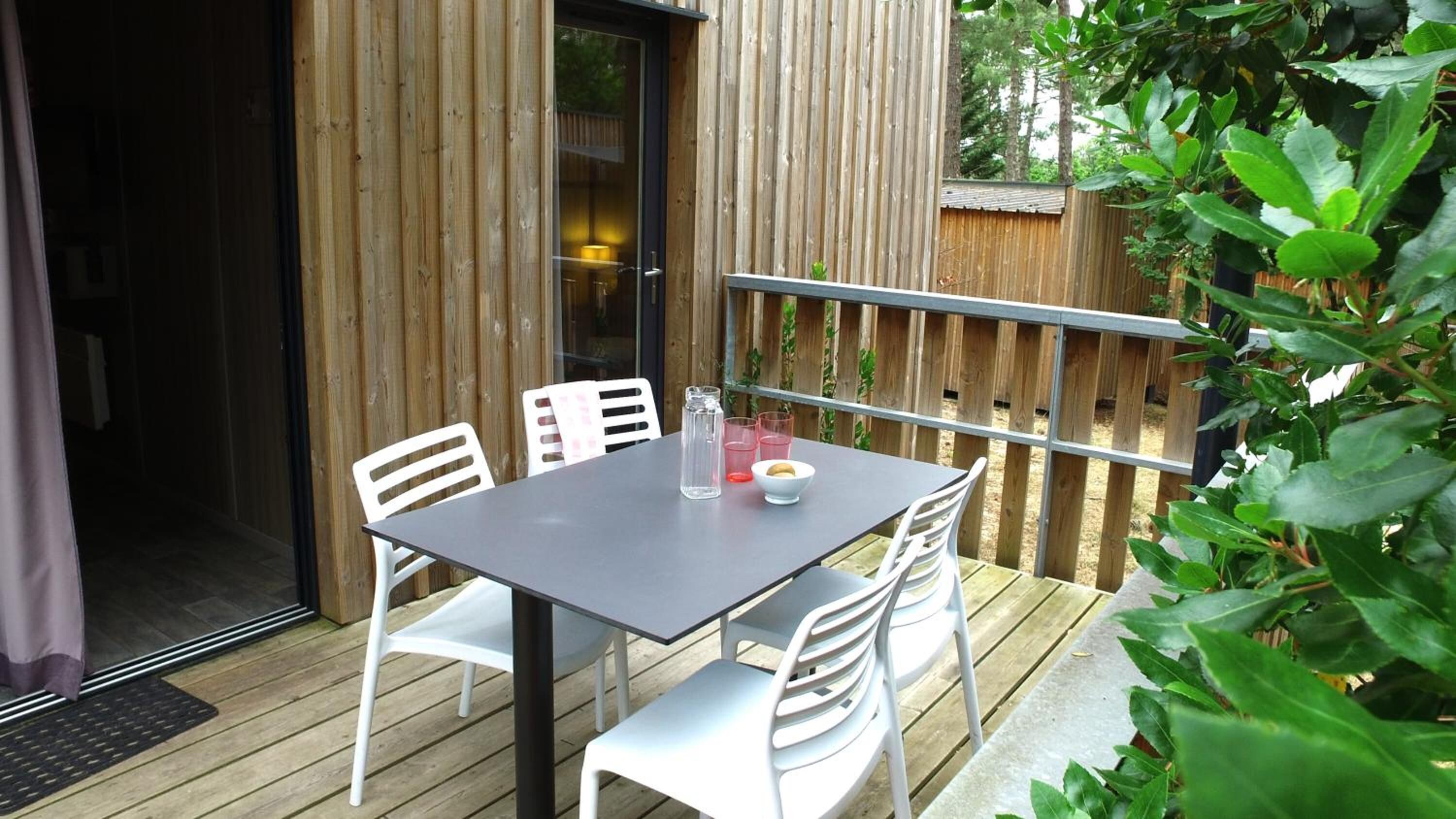 An outdoor patio with a table and chairs, a wooden fence, and greenery.