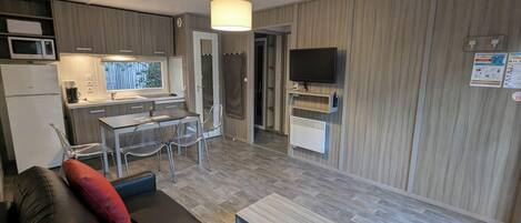 Un espace de vie compact comprenant un coin cuisine, un coin repas, un coin salon avec un canapé et un téléviseur fixé au mur.