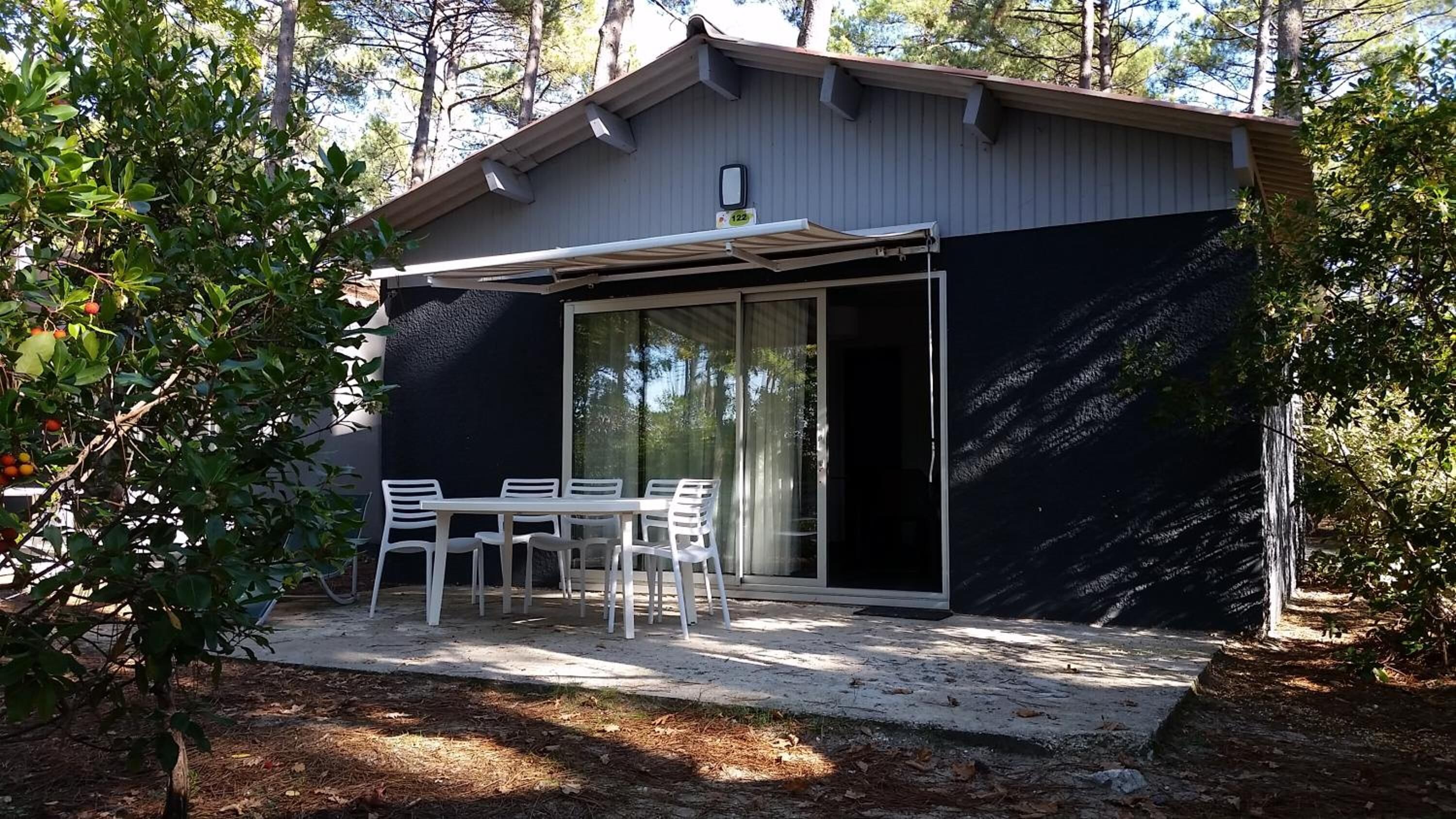 En lille, moderne bygning med en overdækket terrasse, skydedør og et bord med stole.