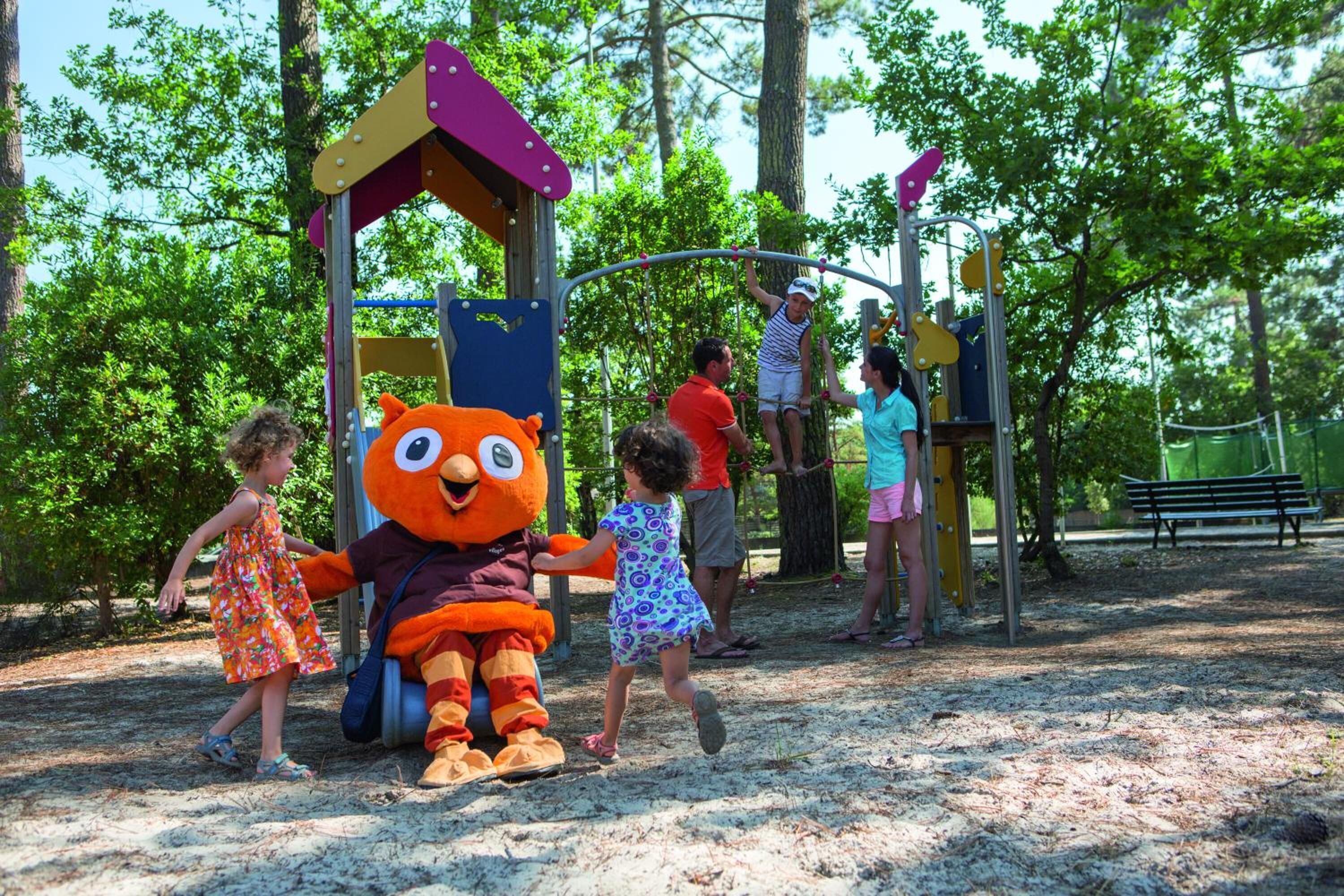 A playground with a large mascot, play structures, and a sandy ground.