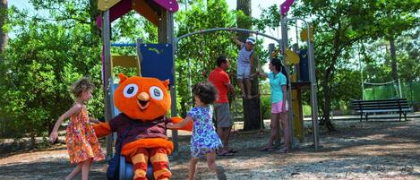 A playground with a large mascot, play structures, and a sandy ground.
