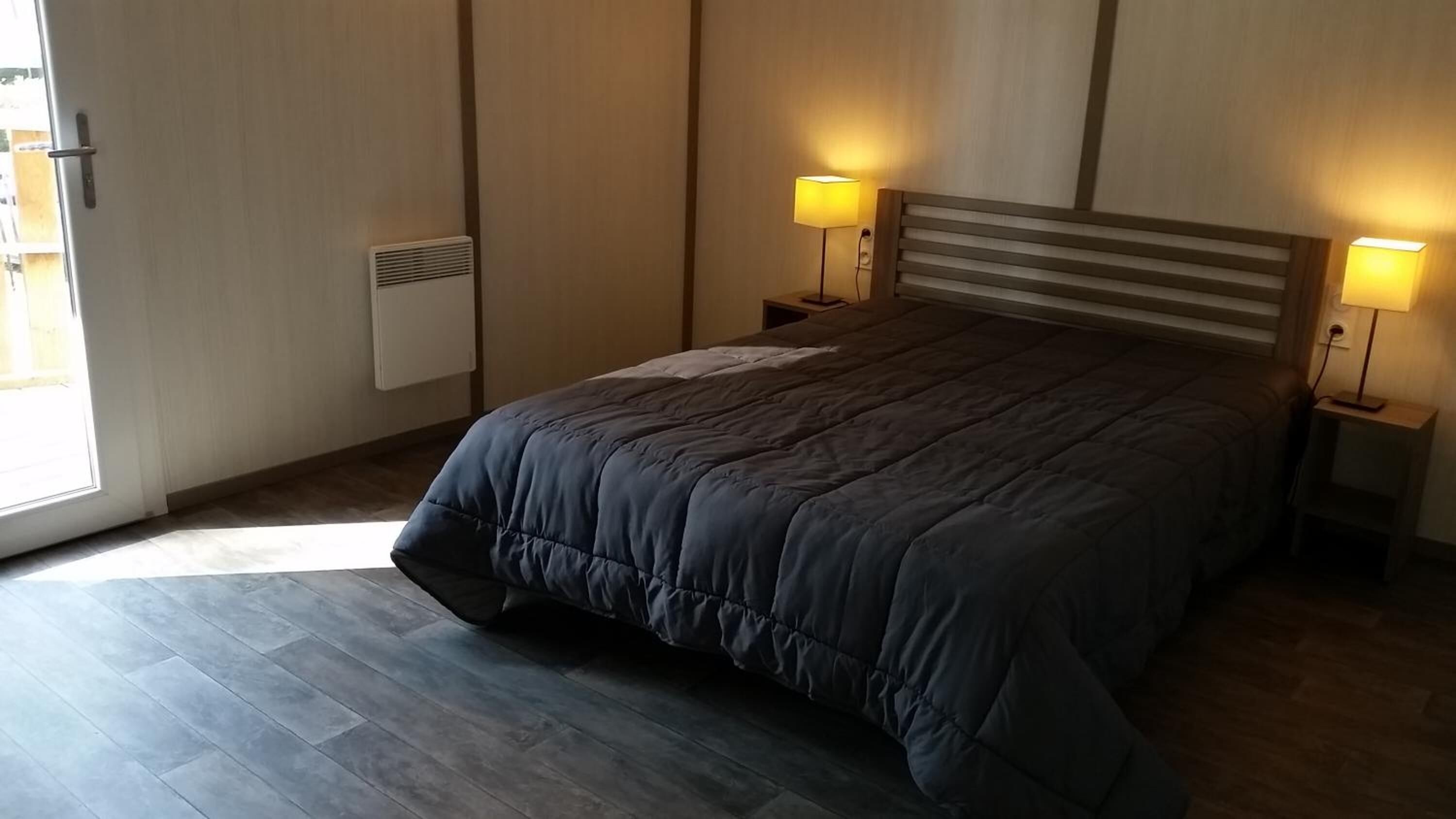 Une chambre avec un grand lit, deux lampes de chevet, un radiateur et une vue sur l’extérieur.