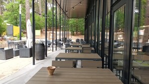 Un espace extérieur aménagé avec des tables et des chaises, entouré d’arbres et doté d’une allée couverte.