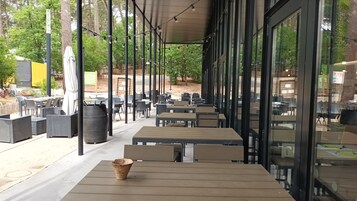 An outdoor seating area with tables and chairs, surrounded by trees and a covered walkway.