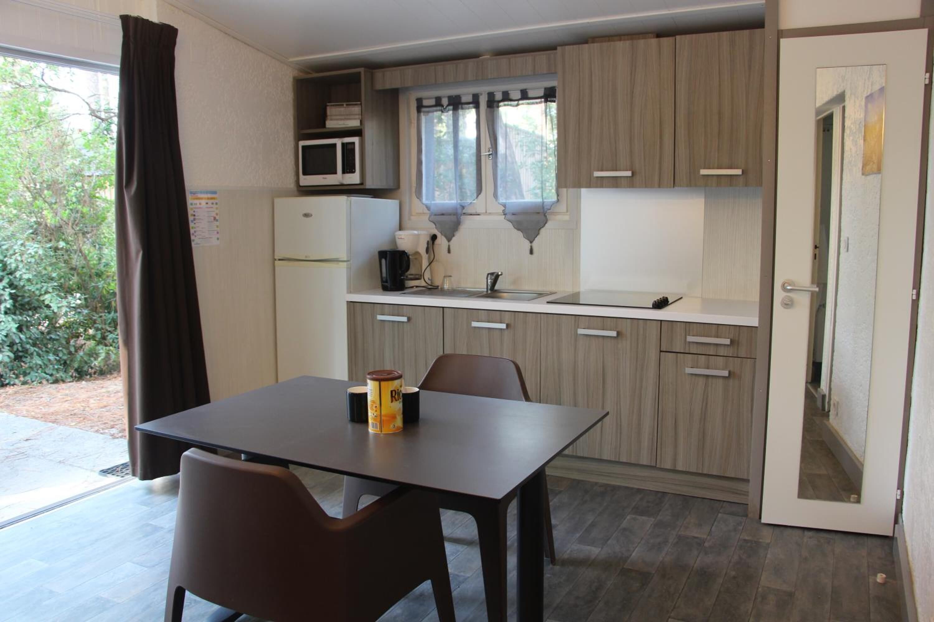 Une cuisine compacte comprenant une table à manger, des chaises, un réfrigérateur, un four à micro-ondes et une fenêtre avec des rideaux.