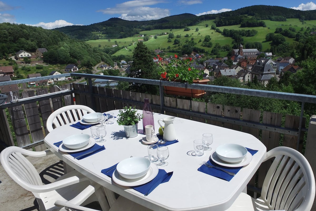 A table set for four with a scenic view of a village and hills in the background.
