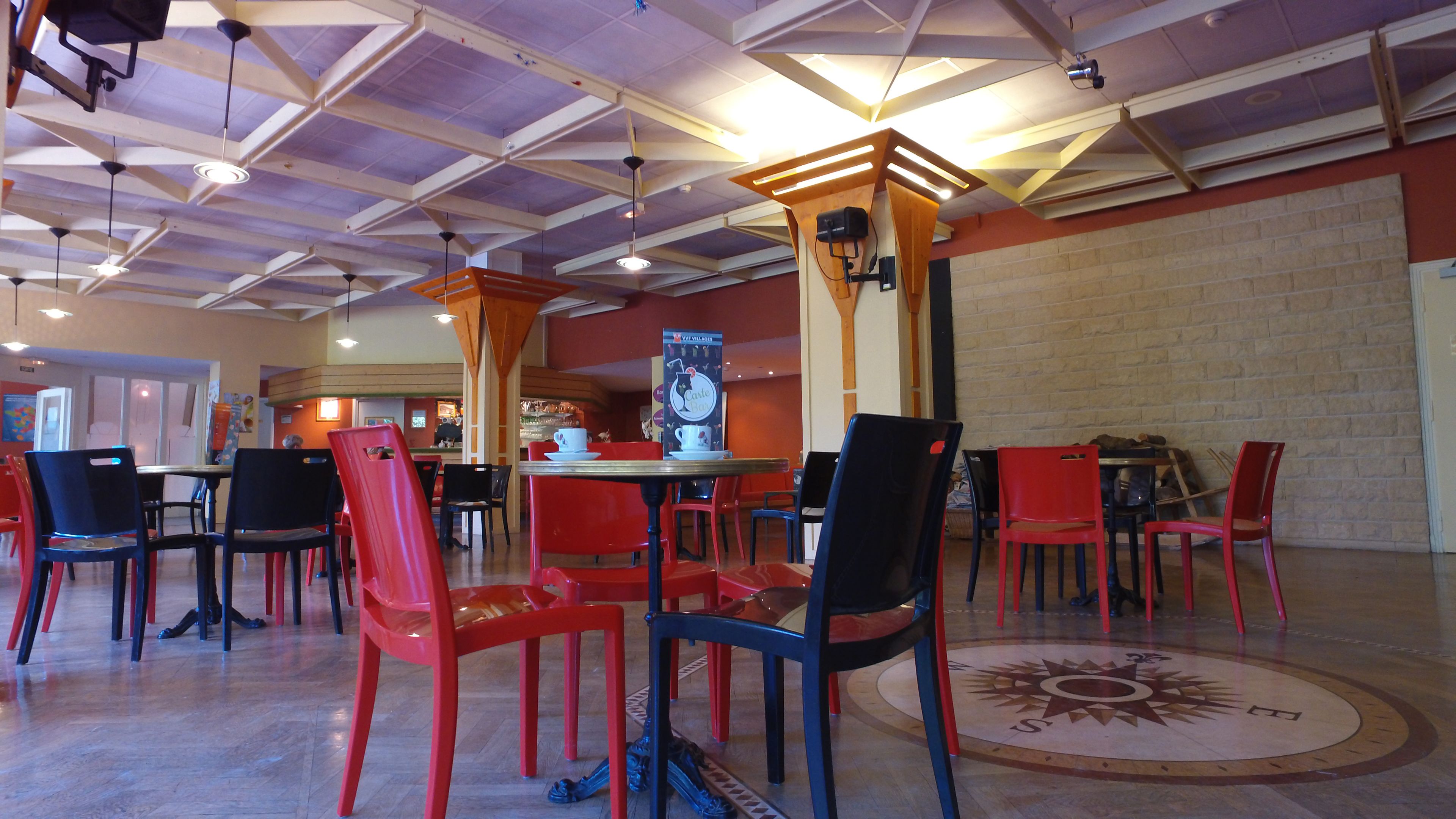 A spacious indoor area with high ceilings, multiple tables and chairs, and a central pillar with a sign.