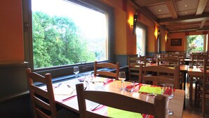 A restaurant with multiple tables and chairs, large windows with a view of greenery outside. - VVF Alsace Orbey Colmar (Orbey)