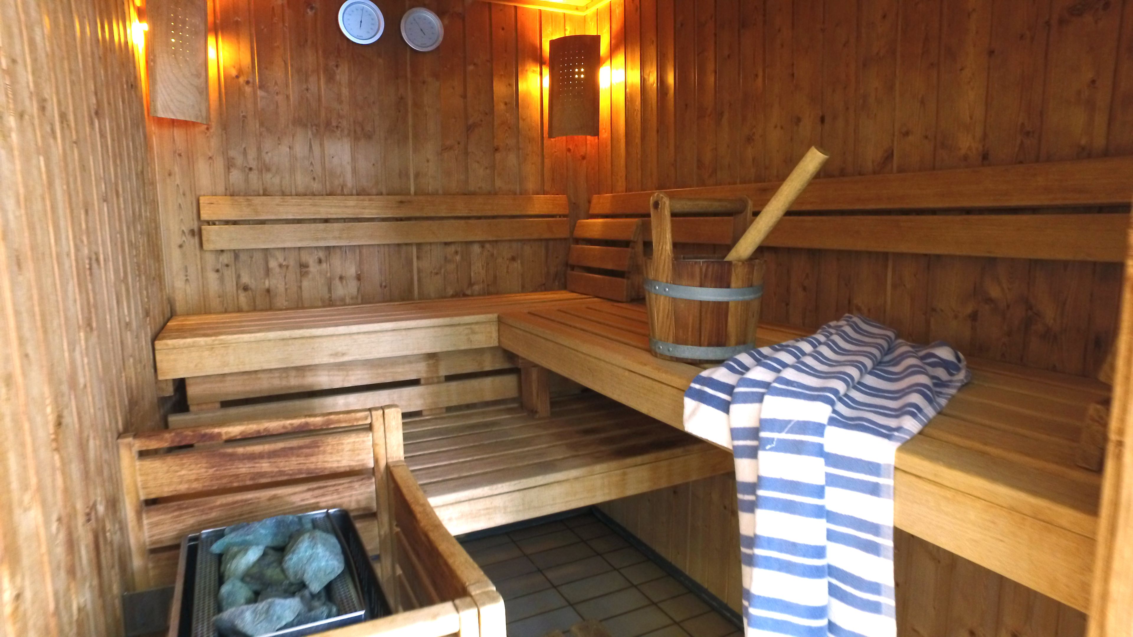 A wooden sauna with benches, a bucket, and a towel.