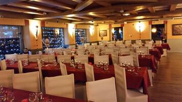 A restaurant with multiple tables set for dining, featuring a view of the cityscape through large windows.