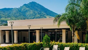 Ein Pool mit Liegestühlen, ein Gebäude mit Säulen und ein Berg im Hintergrund.