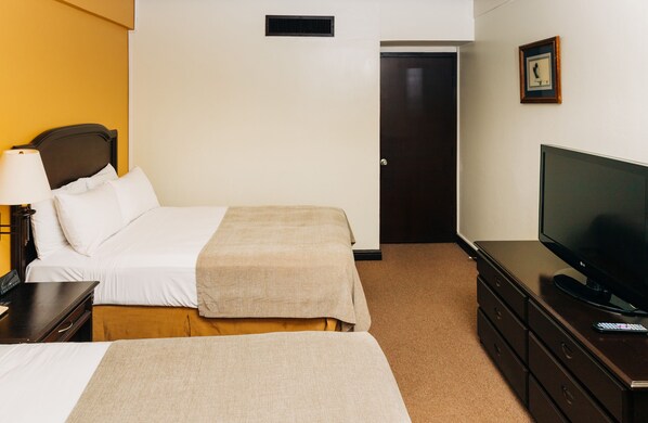 A hotel room with two beds, a television, a dresser, and a door.