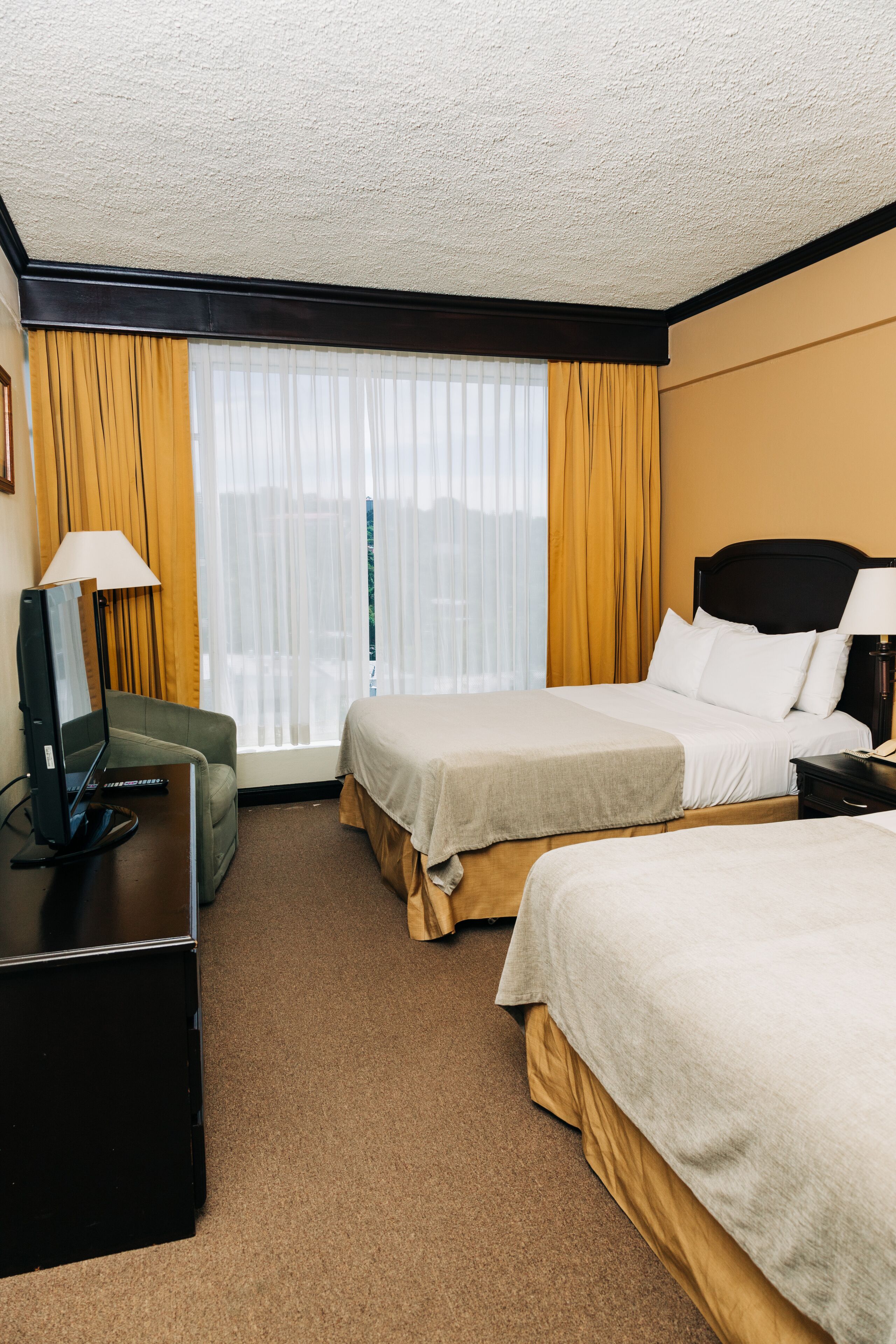 Habitación de hotel con dos camas, un escritorio con computadora, una silla y una ventana con cortinas.