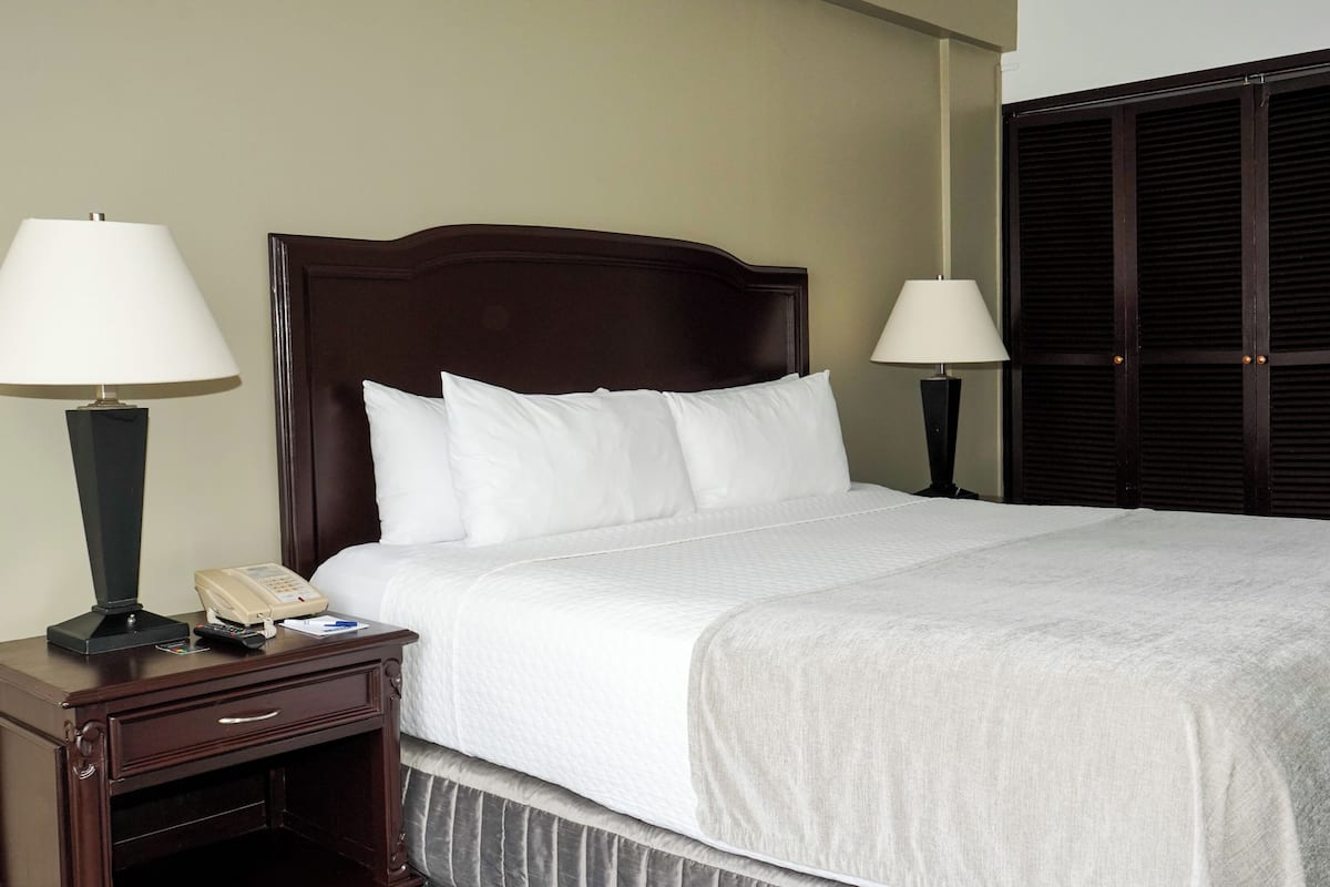 Una cama bien tendida con sábanas blancas, dos lámparas de noche, una mesita de noche de madera con un teléfono y un armario de madera oscura.