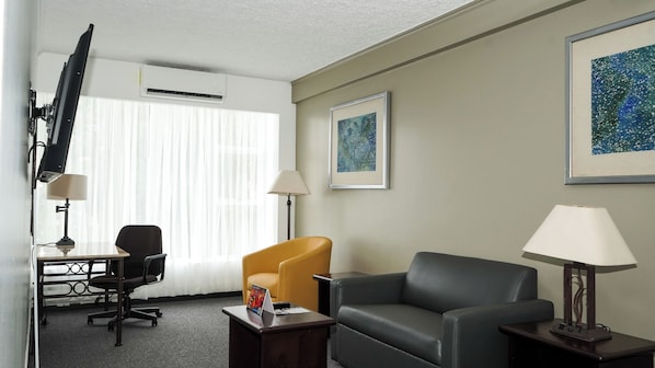 A hotel room with a desk, two chairs, a TV, and artwork on the walls.