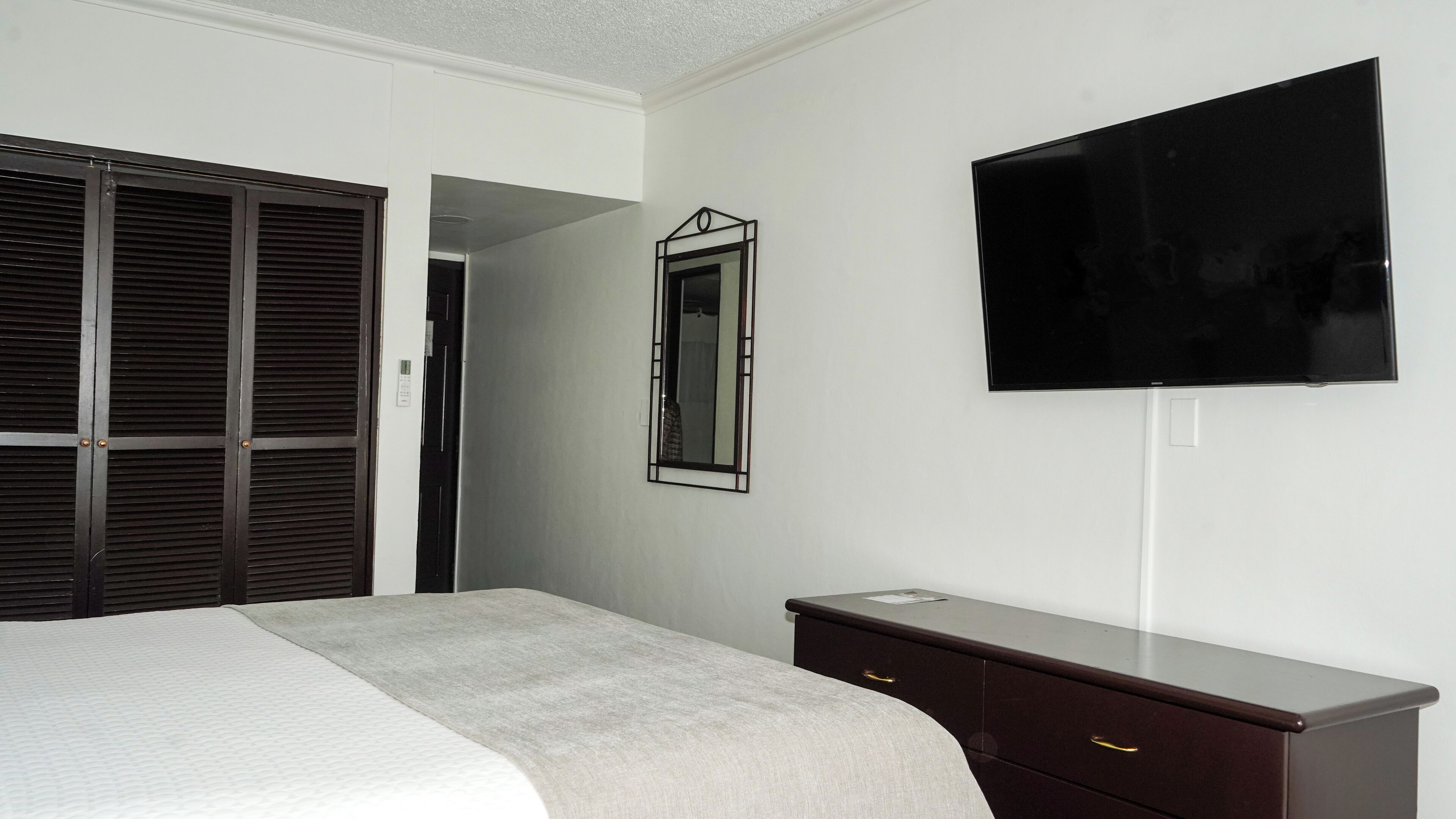 Une chambre d’hôtel équipée d’un lit, d’une commode, d’un miroir et d’un téléviseur à écran plat fixé au mur.