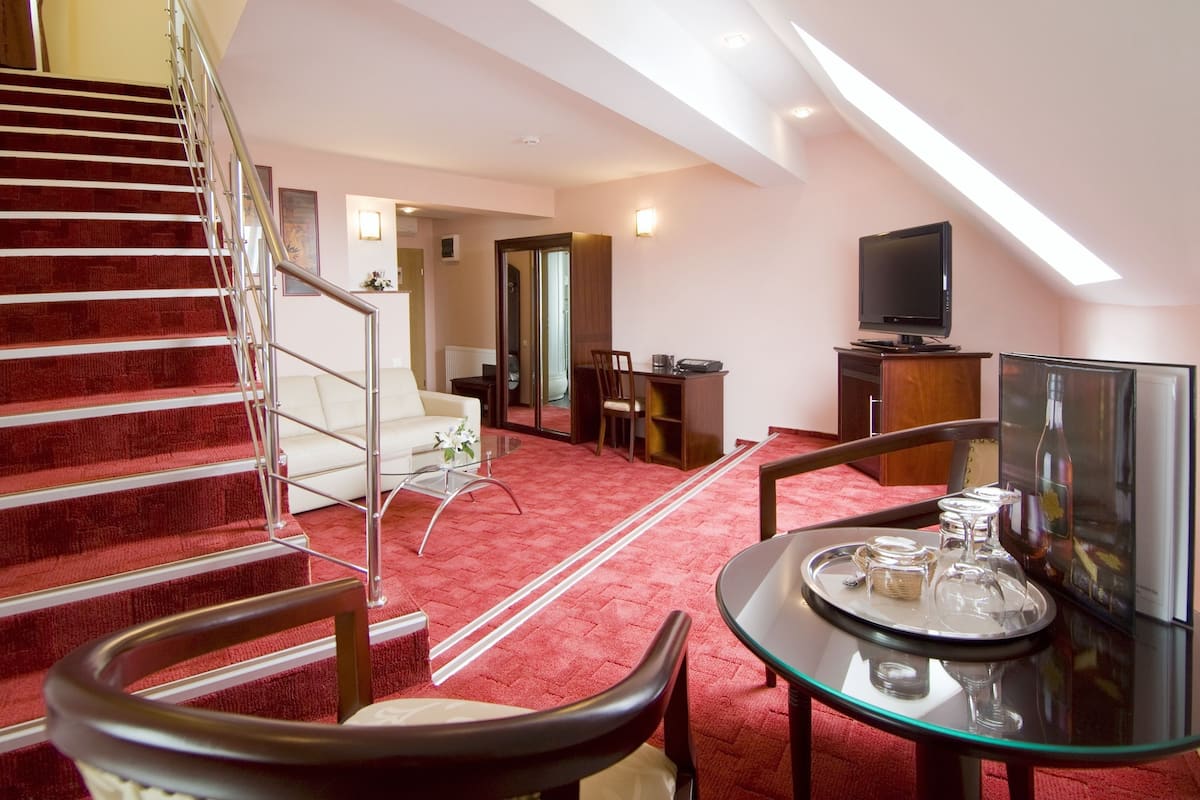 A modern living room with a red carpeted staircase, a glass coffee table with wine glasses, a TV, and a dining area with a white sofa and chairs.